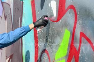 un' mano con un' spray può quello disegna un' nuovo graffiti su il parete. foto di il processi di disegno un' graffiti su un' metallo parete. il concetto di strada arte e illegale vandalismo