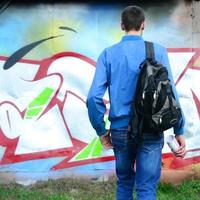 un' giovane graffiti artista con un' nero Borsa sembra a il parete con il suo graffiti su un' parete. strada arte concetto foto