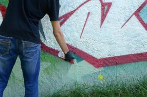 un' giovane teppista vernici graffiti su un' calcestruzzo parete. illegale vandalismo concetto. strada arte foto