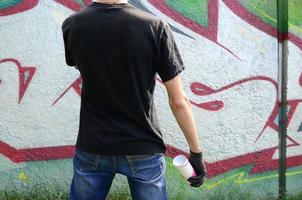 un' giovane teppista con un' spray può sta contro un' calcestruzzo parete con graffiti quadri. illegale vandalismo concetto. strada arte foto