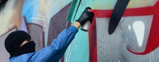 un' giovane teppista con un' nascosto viso vernici graffiti su un' metallo parete. illegale vandalismo concetto foto