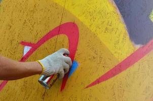 un' mano con un' spray può quello disegna un' nuovo graffiti su il parete. foto di il processi di disegno un' graffiti su un' di legno parete avvicinamento. il concetto di strada arte e illegale vandalismo