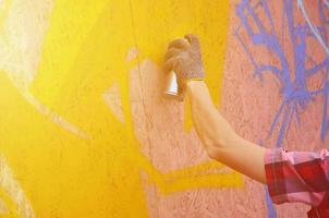 un' mano con un' spray può quello disegna un' nuovo graffiti su il parete. foto di il processi di disegno un' graffiti su un' di legno parete avvicinamento. il concetto di strada arte e illegale vandalismo