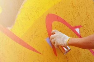 un' mano con un' spray può quello disegna un' nuovo graffiti su il parete. foto di il processi di disegno un' graffiti su un' di legno parete avvicinamento. il concetto di strada arte e illegale vandalismo