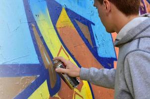 un' giovane dai capelli rossi graffiti artista vernici un' nuovo graffiti su il parete. foto di il processi di disegno un' graffiti su un' parete avvicinamento. il concetto di strada arte e illegale vandalismo