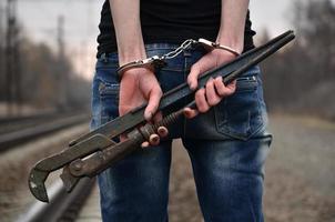 il ragazza nel manette con il tubo chiave inglese su il ferrovia traccia sfondo. il concetto di crimine prevenzione con il partecipazione di il ferrovia e treni. foto