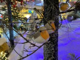 nuovo anno vacanza carta con uccello uccello sospeso piume e Ali diffusione a il bicchiere palla su il ramo di un' abete albero nel il inverno neve parco. foto