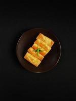 mini martabak guarnito con verde chili peperoni su il Marrone ceramica piatto con nero sfondo foto