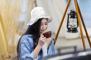 asiatico donna è potabile caffè a sua tenda mentre campeggio all'aperto durante estate tempo nel nazionale parco per avventura e attivo viaggio concetto foto