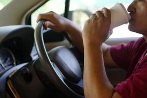 avvicinamento uomo bevanda caffè a partire dal carta tazza nel macchina. concetto, baverge per rinfrescante o porzione per sveglio a partire dal addormentato durante guida quello può causa auto incidente. foto