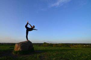 silhouette di giovane bionda ragazza nel sport completo da uomo pratica yoga su un' pittoresco verde collina nel il sera a tramonto. il concetto di esercizio e salutare stili di vita foto