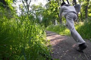 un' giovane tipo nel un' grigio gli sport completo da uomo corre lungo il sentiero tra il foto