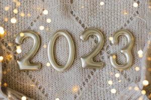 numeri 2023 fatto di d'oro numero su beige a maglia maglione come sfondo. contento nuovo anno 2022, Natale, accogliente vacanza concetti. superiore Visualizza, piatto posare foto