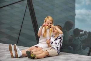 contento biondo donna e poco ragazzo seduta su terrazza e mangiare dolci. madre e figlio godere tempo insieme. positivo giovane mamma giocando, la spesa tempo con sua carino bambino, ridendo, avendo divertimento. famiglia. foto