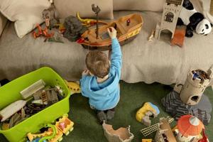 poco caucasico ragazzo con blu felpa con cappuccio giocando con colorato giocattoli a casa. bambino avendo divertimento. contento e allegro ragazzo giochi con nave, dinosauri, castello. tempo libero attività, domestico vita. accogliente camera. foto