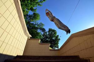 un' giovane tipo esegue un' saltare attraverso il spazio fra il calcestruzzo parapetti. il atleta pratiche parkour, formazione nel strada condizioni. parte inferiore Visualizza foto