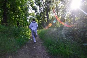 un' giovane tipo nel un' grigio gli sport completo da uomo corre lungo il sentiero tra il foto