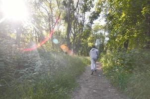 un' giovane tipo nel un' grigio gli sport completo da uomo corre lungo il sentiero tra il foto