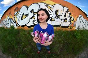 ritratto di un emotivo giovane ragazza con nero capelli e piercing. un' angolo ampio foto di un' ragazza con aerosol dipingere lattine nel il mani su un' graffiti parete sfondo. un' moderno ritratto di un' fisheye lente