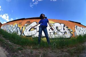 ritratto di un emotivo giovane ragazza con nero capelli e piercing. un' angolo ampio foto di un' ragazza con aerosol dipingere lattine nel il mani su un' graffiti parete sfondo. un' moderno ritratto di un' fisheye lente