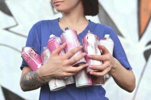 ritratto di un emotivo giovane ragazza con nero capelli e piercing. foto di un' ragazza con aerosol dipingere lattine nel mani su un' graffiti parete sfondo. il concetto di strada arte e uso di aerosol vernici