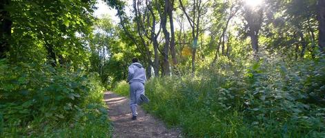 un' giovane tipo nel un' grigio gli sport completo da uomo corre lungo il sentiero tra il foto