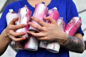 ritratto di un emotivo giovane ragazza con nero capelli e piercing. foto di un' ragazza con aerosol dipingere lattine nel mani su un' graffiti parete sfondo. il concetto di strada arte e uso di aerosol vernici