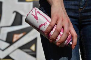 foto di un' ragazze mano con aerosol dipingere lattine nel mani su un' graffiti parete sfondo. il concetto di strada arte e uso di aerosol vernici. graffiti arte negozio sfondo Immagine