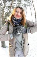un' giovane e gioioso caucasico ragazza nel un' Marrone cappotto scolpisce un' palla di neve nel un' innevato foresta nel inverno. Giochi con neve nel il Aperto aria. fisheye foto