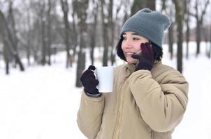 inverno ritratto di giovane ragazza con smartphone e caffè tazza foto