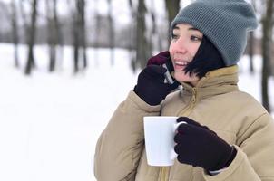 inverno ritratto di giovane ragazza con smartphone e caffè tazza foto