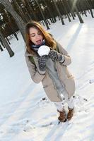 un' giovane e gioioso caucasico ragazza nel un' Marrone cappotto detiene un' palla di neve nel un' innevato foresta nel inverno. fisheye foto