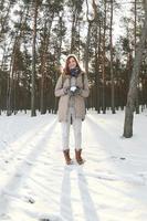 un' giovane e gioioso caucasico ragazza nel un' Marrone cappotto detiene un' palla di neve nel un' innevato foresta nel inverno. fisheye foto