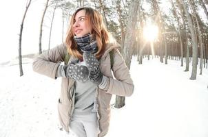 un' giovane e gioioso caucasico ragazza nel un' Marrone cappotto scolpisce un' palla di neve nel un' innevato foresta nel inverno. Giochi con neve nel il Aperto aria. fisheye foto