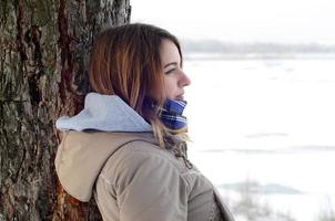 un' giovane caucasico ragazza nel un' Marrone cappotto fissando in il distanza su il orizzonte linea fra il cielo e il congelato lago nel inverno foto