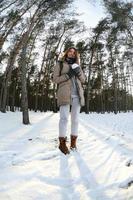 un' giovane e gioioso caucasico ragazza nel un' Marrone cappotto detiene un' palla di neve nel un' innevato foresta nel inverno. fisheye foto