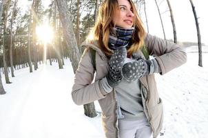 un' giovane e gioioso caucasico ragazza nel un' Marrone cappotto scolpisce un' palla di neve nel un' innevato foresta nel inverno. Giochi con neve nel il Aperto aria. fisheye foto