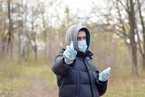 giovane uomo nel protettivo maschera Spettacoli disinfettante spray bottiglie all'aperto nel primavera legna foto