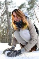 un' giovane e gioioso caucasico ragazza nel un' Marrone cappotto scolpisce un' palla di neve nel un' innevato foresta nel inverno. Giochi con neve nel il Aperto aria. fisheye foto