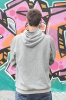 un' giovane graffiti artista nel un' grigio felpa con cappuccio sembra a il parete con foto