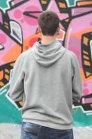 un' giovane graffiti artista nel un' grigio felpa con cappuccio sembra a il parete con foto