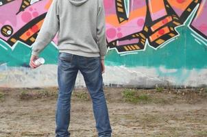 un' giovane graffiti artista nel un' grigio felpa con cappuccio sembra a il parete con foto