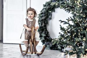 un' poco ragazza altalene su un' di legno cavallo nel il camera contro il sfondo di Natale decorazioni. foto