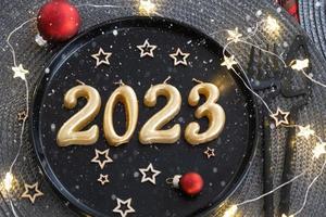 d'oro figure 2023 a partire dal candele su un' nero piatto su un' festivo tavolo con un' nuovo anni servendo. in stile loft interno, festa, festa. di vimini tovagliolo, forchetta, coltello foto