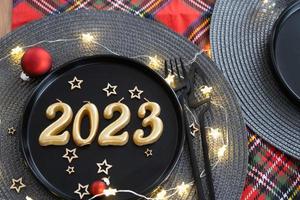 d'oro figure 2023 a partire dal candele su un' nero piatto su un' festivo tavolo con un' nuovo anni servendo. in stile loft interno, festa, festa. di vimini tovagliolo, forchetta, coltello foto