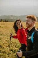 coppia sorridente che cammina con zaini su verdi colline foto