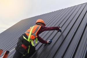 sfondo roofer lavoratore nel protettivo uniforme indossare e guanti, coperture strumenti, installazione nuovo tetti sotto costruzione, elettrico trapano Usato su nuovo tetti con metallo foglio. foto