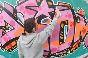 un' giovane tipo nel un' grigio felpa con cappuccio vernici graffiti nel rosa e verde c foto