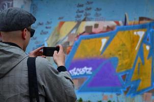 un' giovane graffiti artista fotografie il suo completato immagine su il parete. il tipo usi moderno tecnologia per catturare un' colorato astratto graffiti disegno. messa a fuoco su il Fotografare dispositivo