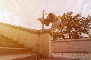 un' giovane tipo esegue un' saltare attraverso il calcestruzzo parapetto. il atleta pratiche parkour, formazione nel strada condizioni. il concetto di gli sport sottoculture tra gioventù foto